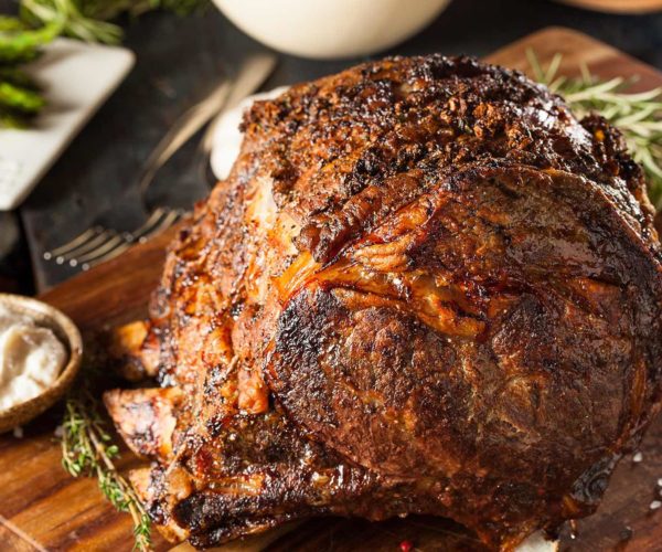 Carré d'agneau rôti présenté sur sa planchette en bois accompagné de sa sauce servi au restaurant la Table de Trois
